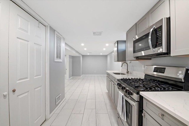 kitchen featuring gray cabinetry, sink, stainless steel appliances, and light stone countertops