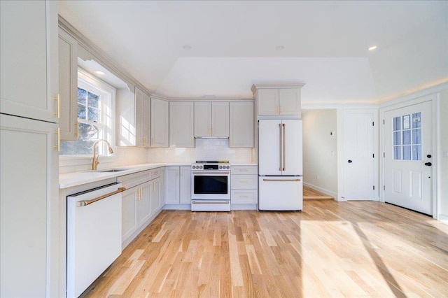 kitchen featuring sink, vaulted ceiling, white appliances, light hardwood / wood-style floors, and backsplash