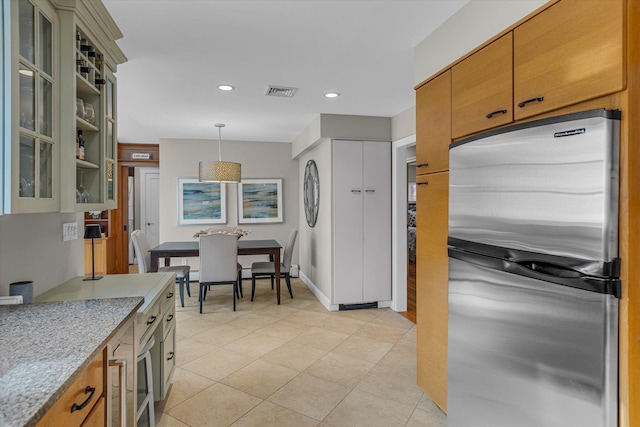 kitchen with light stone countertops, pendant lighting, and stainless steel fridge