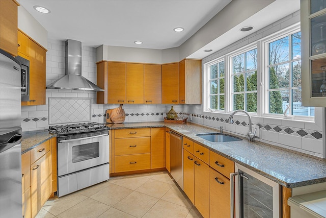 kitchen featuring wall chimney range hood, sink, stone counters, stainless steel appliances, and beverage cooler