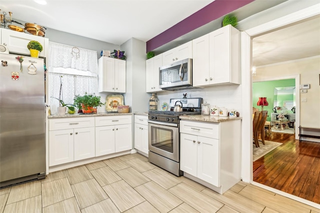 kitchen with white cabinetry, backsplash, light stone counters, and stainless steel appliances