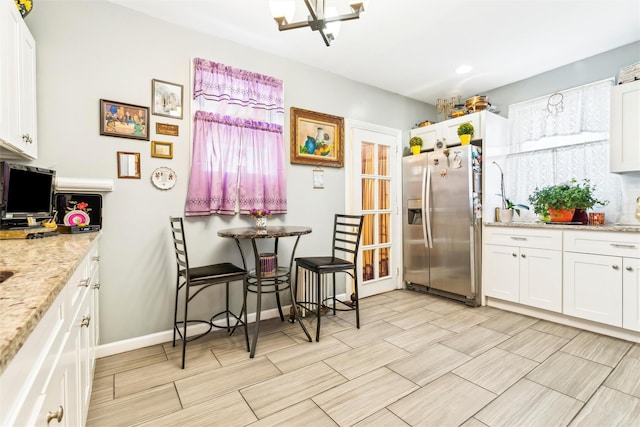 kitchen with white cabinetry, stainless steel fridge, light stone countertops, and a notable chandelier