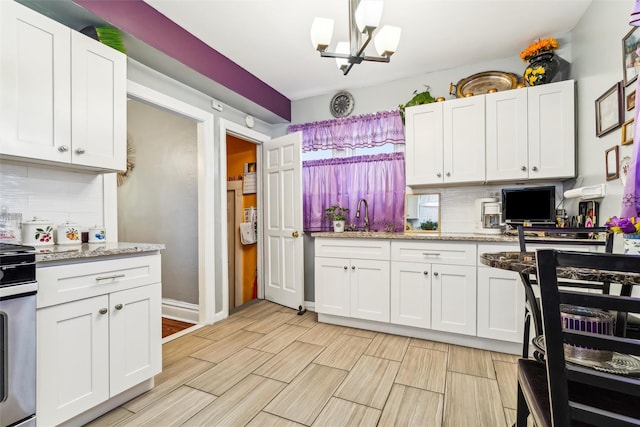 kitchen with white cabinetry, a chandelier, light stone counters, and decorative backsplash