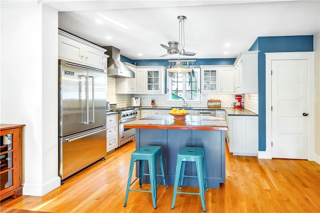 kitchen with high end appliances, wall chimney range hood, white cabinetry, and a center island