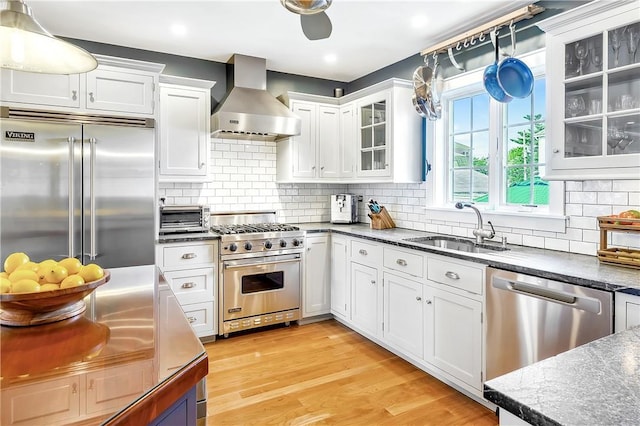 kitchen featuring white cabinetry, sink, wall chimney range hood, and premium appliances