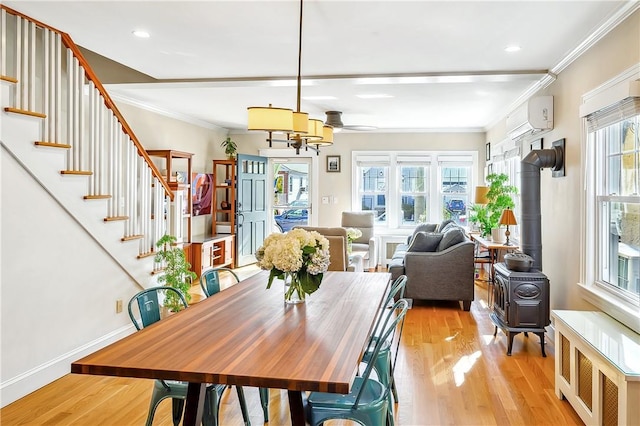 dining space featuring crown molding, a wall mounted AC, light wood-type flooring, a wood stove, and radiator heating unit