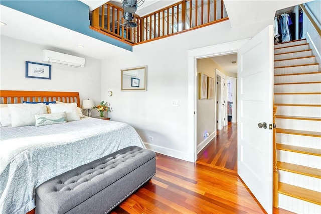 bedroom with a wall mounted air conditioner, wood-type flooring, and a high ceiling