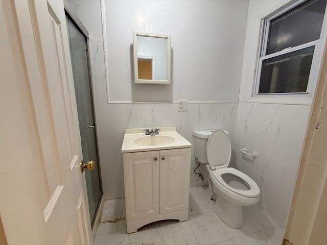 bathroom featuring a shower with door, vanity, tile walls, and toilet