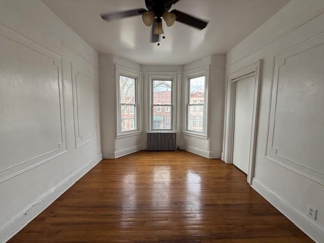 unfurnished room featuring hardwood / wood-style flooring, ceiling fan, and radiator