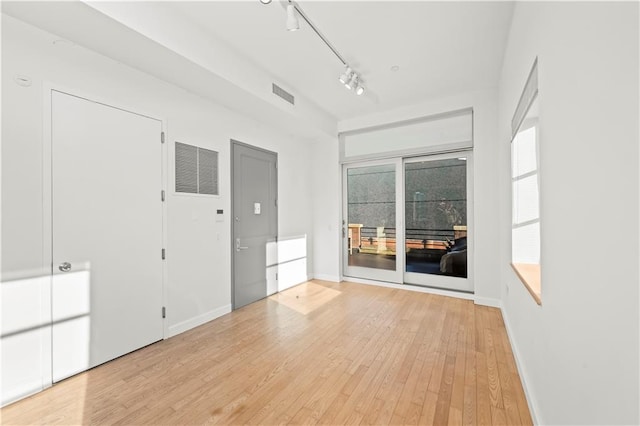 spare room featuring baseboards, light wood-style flooring, visible vents, and track lighting