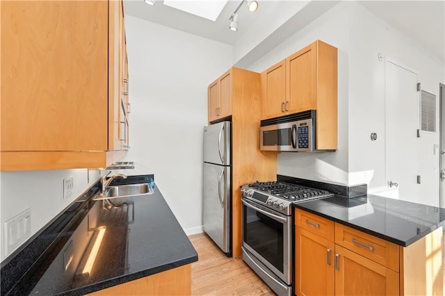 kitchen featuring a skylight, light wood finished floors, stainless steel appliances, a sink, and dark stone countertops