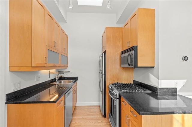 kitchen featuring light wood finished floors, baseboards, dark stone counters, appliances with stainless steel finishes, and a sink