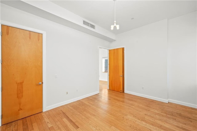 empty room featuring baseboards, a chandelier, visible vents, and light wood-style floors