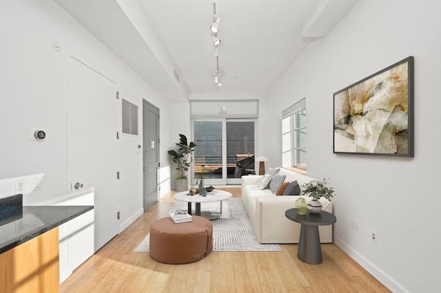 living area with light wood finished floors, track lighting, visible vents, and baseboards