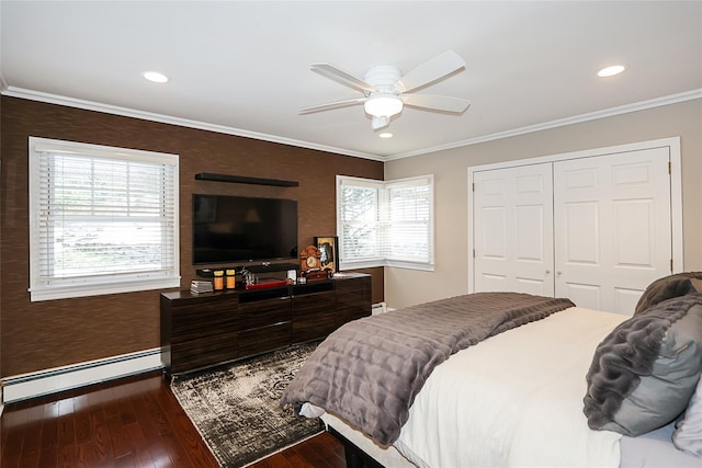 bedroom with crown molding, dark wood-type flooring, ceiling fan, a baseboard heating unit, and a closet