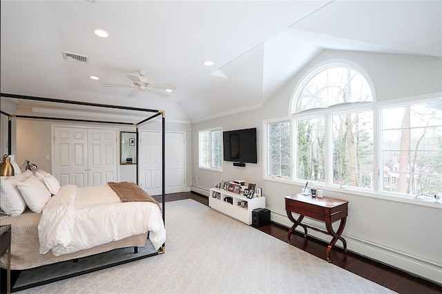 bedroom with wood-type flooring, lofted ceiling, a baseboard heating unit, and two closets