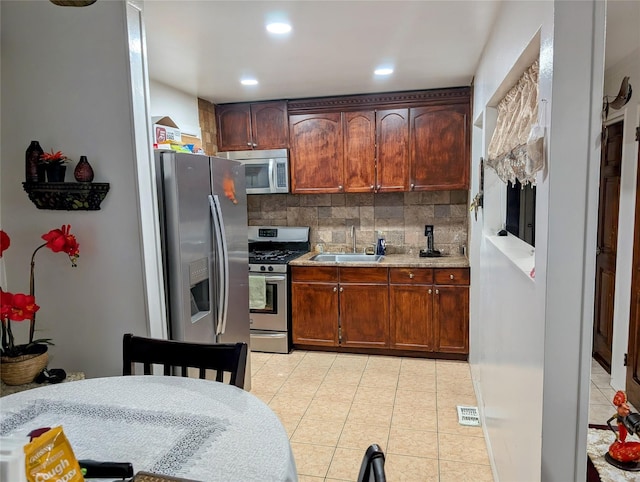 kitchen with a sink, light countertops, appliances with stainless steel finishes, decorative backsplash, and light tile patterned flooring