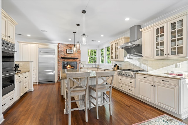 kitchen with hanging light fixtures, a center island with sink, appliances with stainless steel finishes, light stone countertops, and cream cabinetry