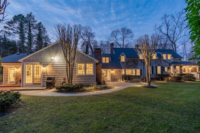 back house at dusk with a patio and a lawn