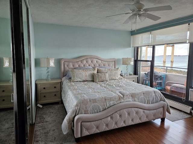 bedroom with ceiling fan, a water view, expansive windows, a textured ceiling, and dark hardwood / wood-style flooring