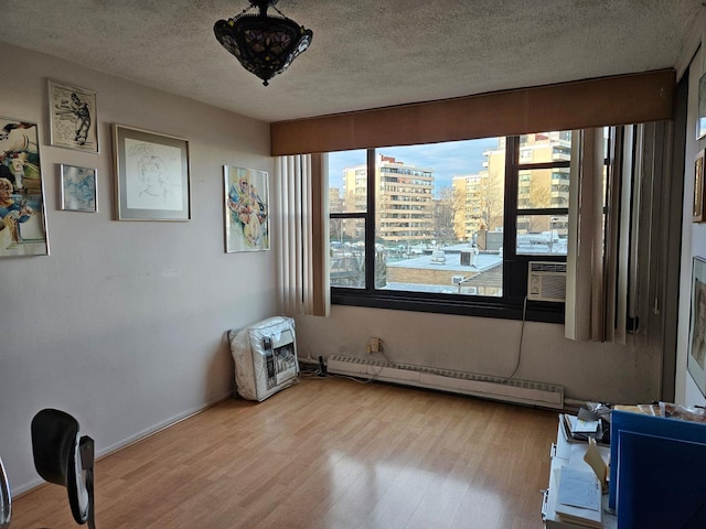 spare room featuring cooling unit, a baseboard heating unit, a textured ceiling, and light wood-type flooring