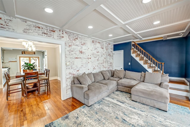 living room with coffered ceiling, a chandelier, ornamental molding, hardwood / wood-style flooring, and brick wall