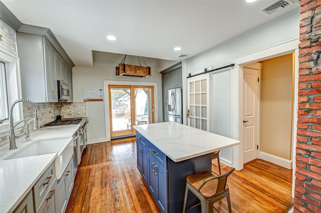 kitchen with sink, backsplash, stainless steel appliances, a barn door, and light wood-type flooring