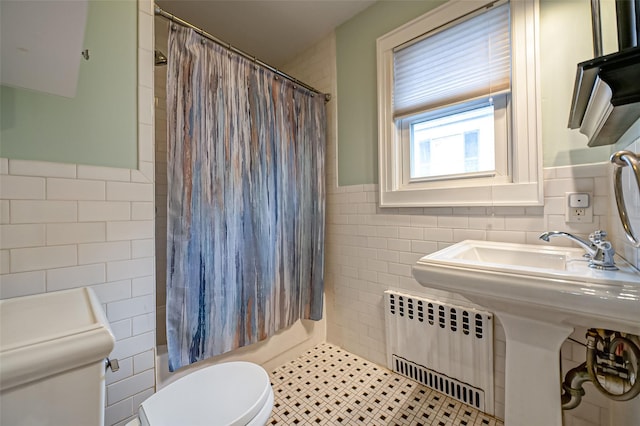 bathroom with radiator heating unit, toilet, tile patterned flooring, and tile walls