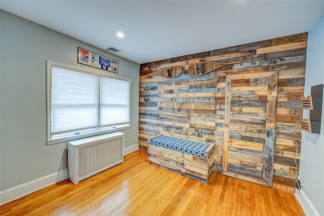 living area with light wood-type flooring, radiator heating unit, and wood walls