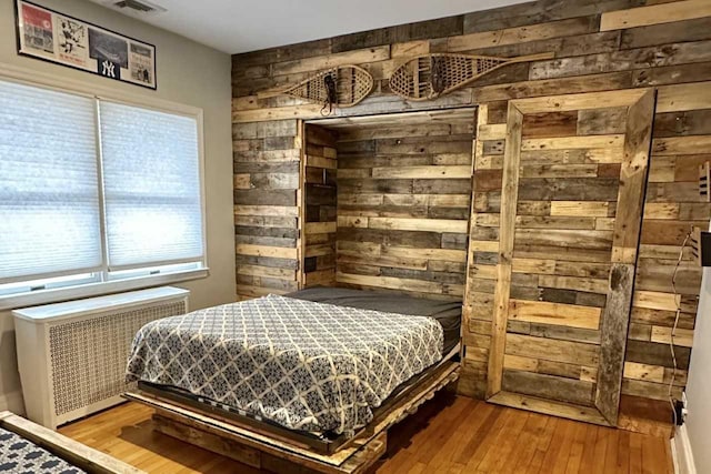 bedroom with multiple windows, wood-type flooring, radiator, and wood walls