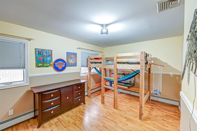 bedroom featuring light hardwood / wood-style floors, multiple windows, and a baseboard heating unit