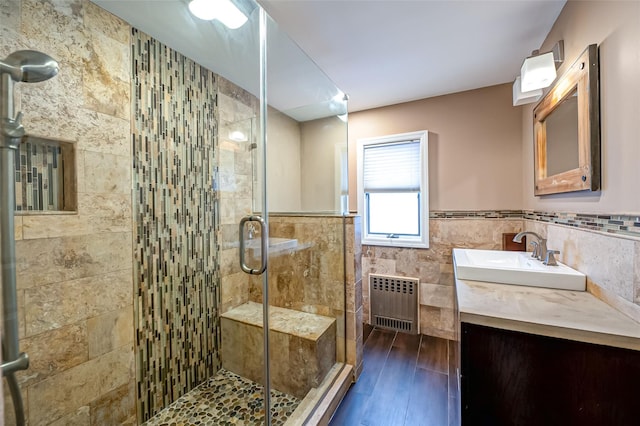 bathroom with radiator, hardwood / wood-style flooring, a shower with door, tile walls, and vanity