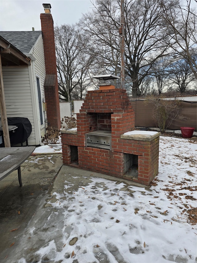 snow covered patio featuring exterior fireplace and a grill