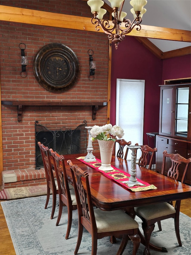 dining space with a notable chandelier, wood-type flooring, lofted ceiling with beams, and a brick fireplace