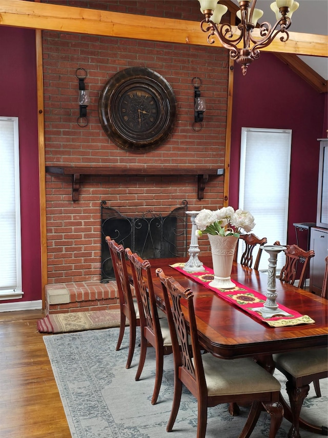 dining room with wood-type flooring, a healthy amount of sunlight, a chandelier, and a fireplace