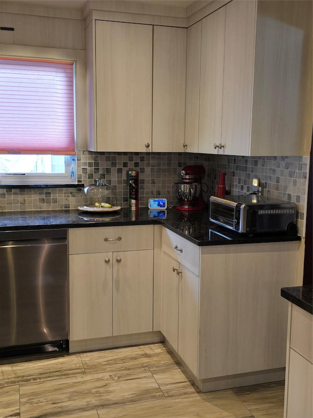 kitchen featuring dark stone countertops, stainless steel dishwasher, backsplash, and light brown cabinetry