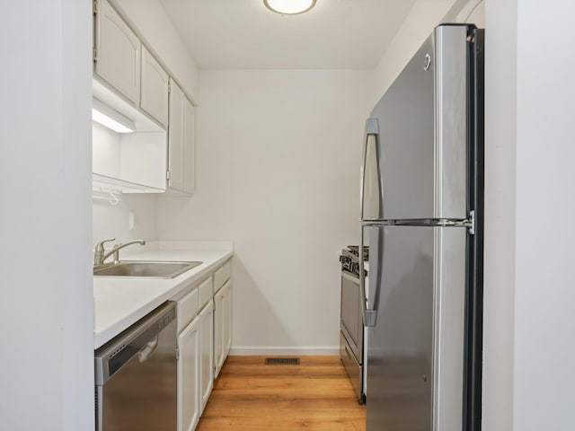 kitchen with sink, stainless steel appliances, white cabinets, and light wood-type flooring