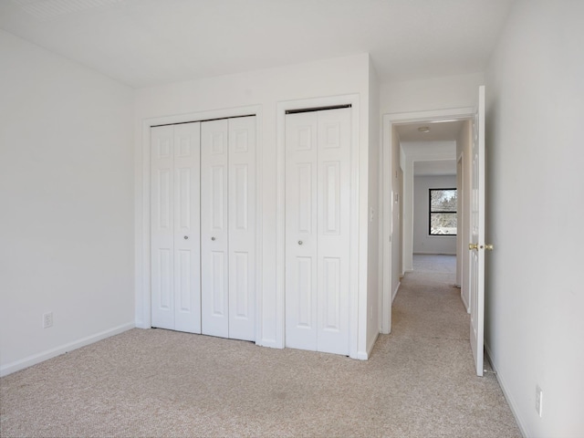 unfurnished bedroom featuring multiple closets and light colored carpet