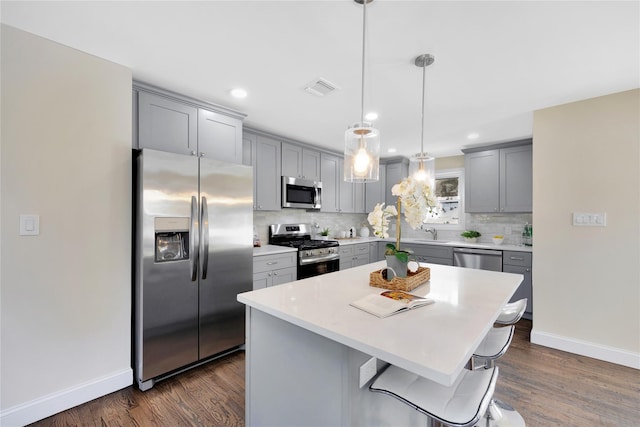 kitchen with dark wood-type flooring, a kitchen bar, a center island, appliances with stainless steel finishes, and pendant lighting