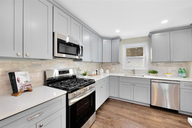 kitchen featuring sink, gray cabinetry, dark hardwood / wood-style flooring, stainless steel appliances, and decorative backsplash