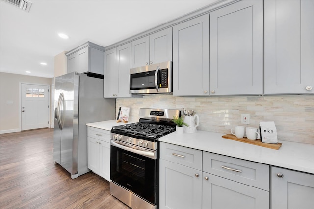 kitchen featuring gray cabinets, tasteful backsplash, appliances with stainless steel finishes, and hardwood / wood-style flooring