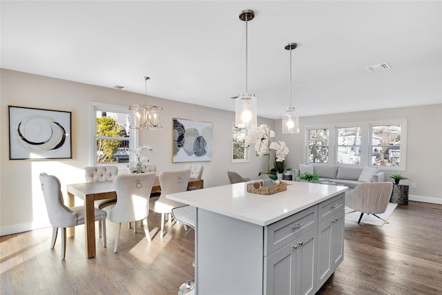 kitchen featuring dark wood-type flooring, gray cabinetry, hanging light fixtures, a kitchen island, and a notable chandelier