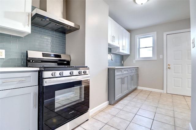 kitchen featuring light tile patterned flooring, wall chimney exhaust hood, stainless steel gas range oven, tasteful backsplash, and white cabinetry