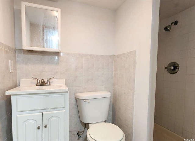 bathroom with vanity, a tile shower, tile walls, and toilet