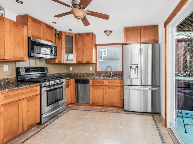 kitchen with appliances with stainless steel finishes, sink, dark stone counters, light tile patterned floors, and ceiling fan