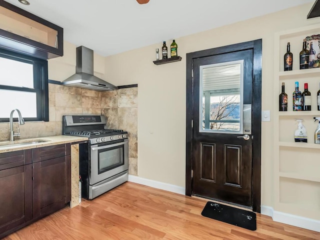 kitchen featuring sink, backsplash, light hardwood / wood-style floors, island exhaust hood, and stainless steel range with gas cooktop