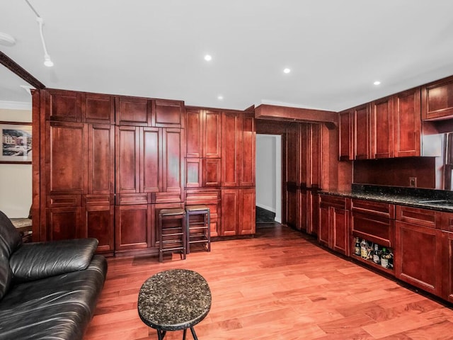 kitchen with dark stone countertops, ornamental molding, and light wood-type flooring