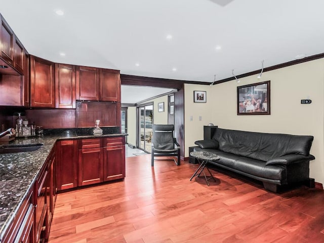 kitchen featuring crown molding, sink, light hardwood / wood-style floors, and dark stone countertops