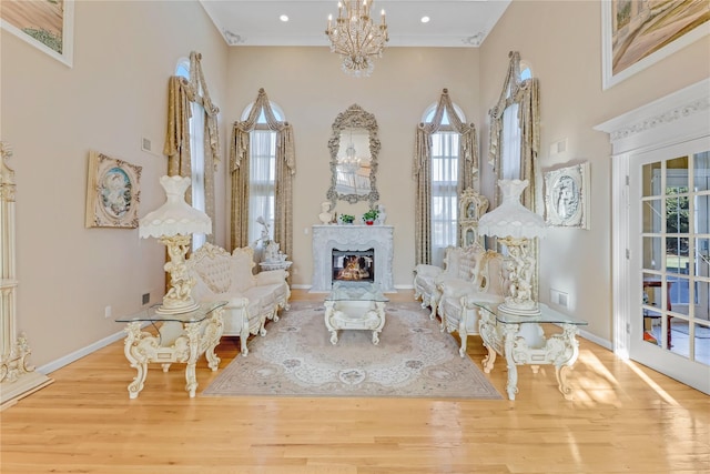 living area with crown molding, a premium fireplace, a high ceiling, light hardwood / wood-style floors, and a chandelier