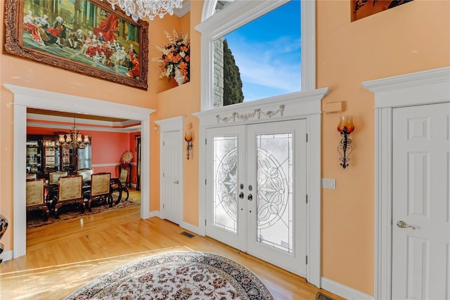 entrance foyer with crown molding, hardwood / wood-style floors, a towering ceiling, french doors, and a chandelier